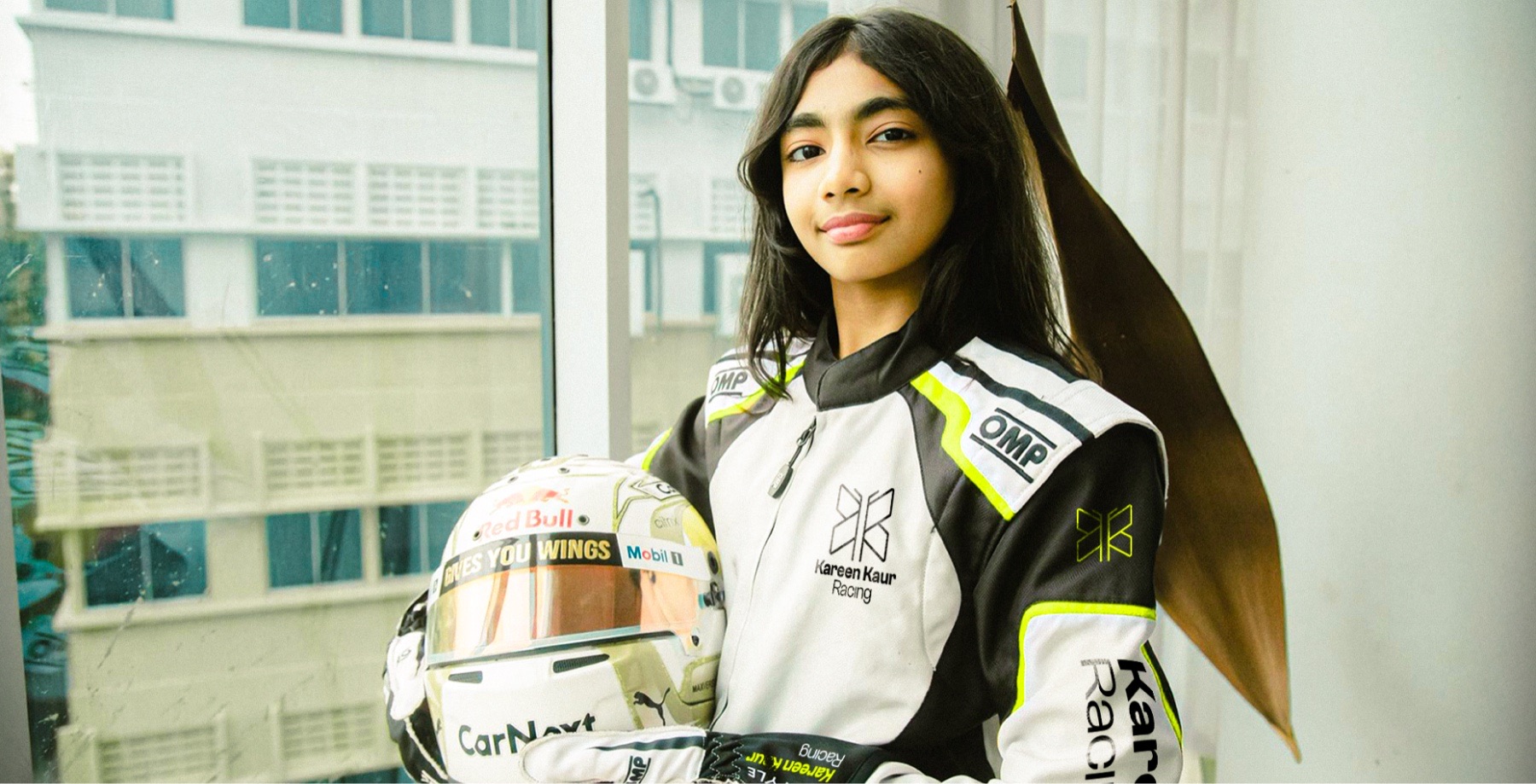 Kareen Kaur standing in a race suit with her helmet under one arm.
