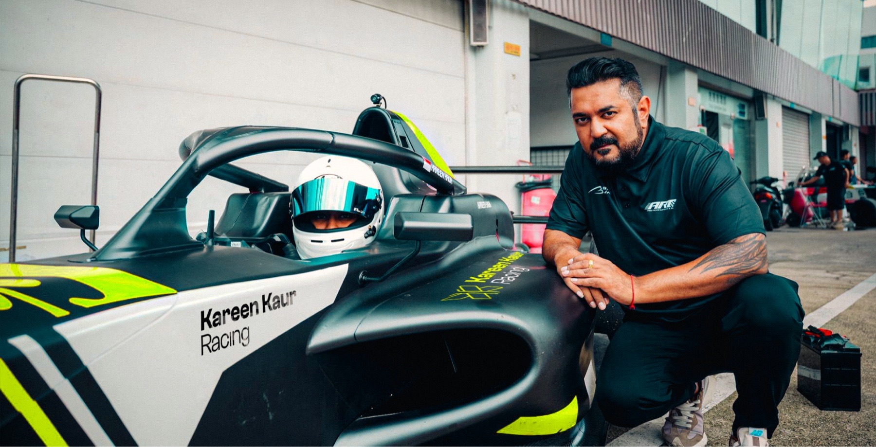 Kareen Kaur seated in the cockpit while a crew member leans against the car.